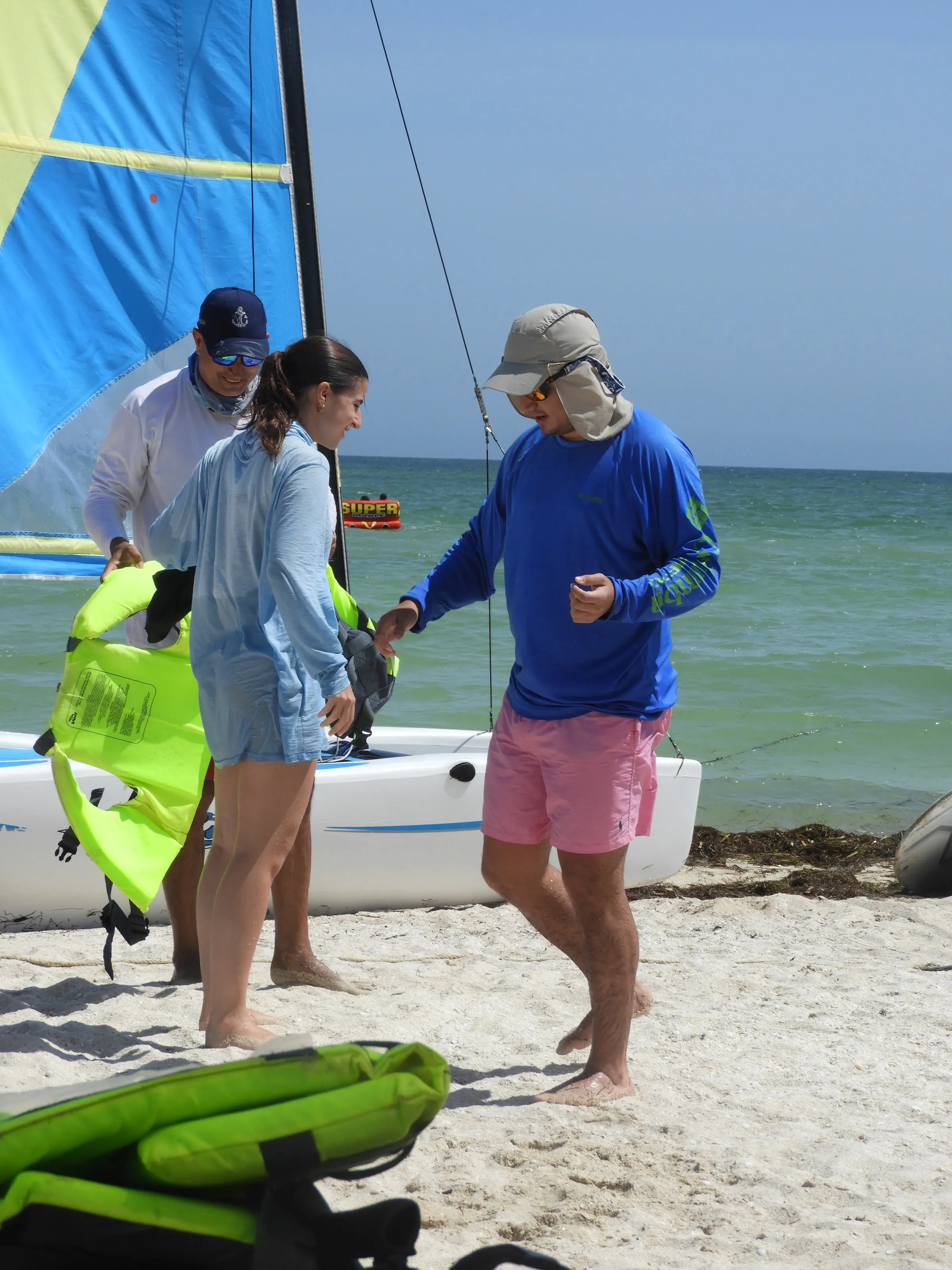 Dos instructores y una joven conversan en la arena junto a un Hobie Cat con la vela izada.